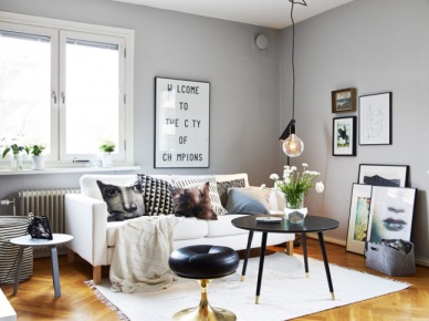 Szare ściany, żarówka na kablu,czarny okragły stolik,gafiki i typografie i drukowane poduszki w salonie skandynawskim (25686)