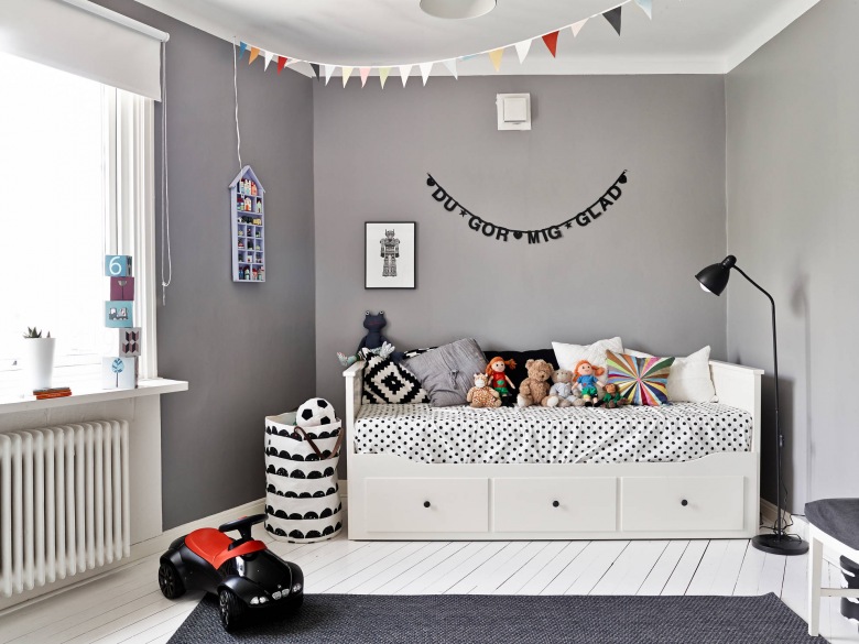 Białe łóżko z szufladami,szara ściana,kolorowe proporczyki girlanda,białe deski na podłodze i biało-czarne dekoracje w pokoju dziecięcym (26772)
