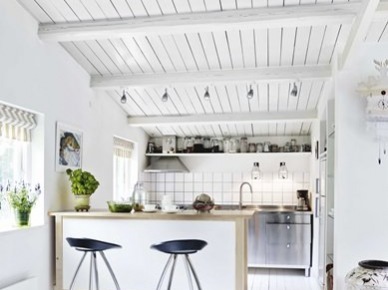 Biała kuchnia w białym domku z kuchenną wyspą na kółkach i czarnymi wysokimi stołkami barowymi na metalowych nogach (26198)