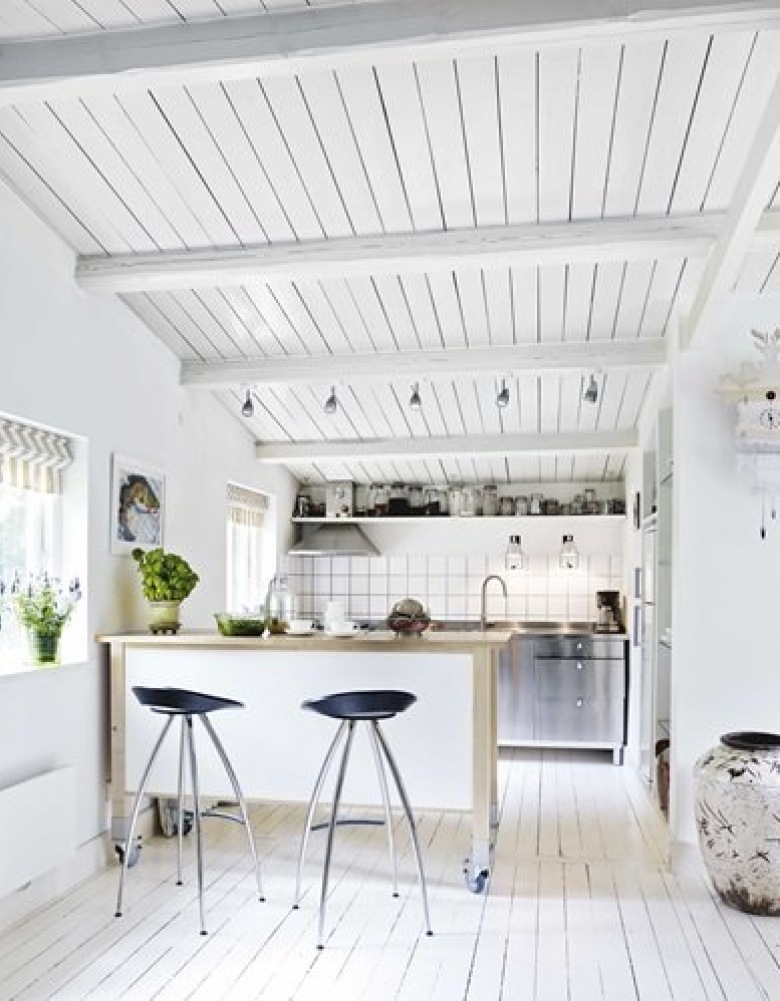 Biała kuchnia w białym domku z kuchenną wyspą na kółkach i czarnymi wysokimi stołkami barowymi na metalowych nogach (26198)