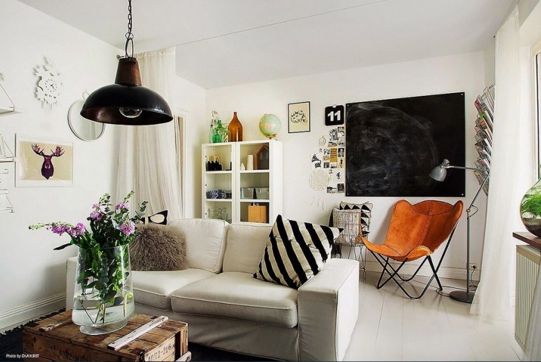 Jasny salon w skandynawskim stylu z szara sofę został skontrastowany przez czarna lampę i tablicę. Poduszka w...