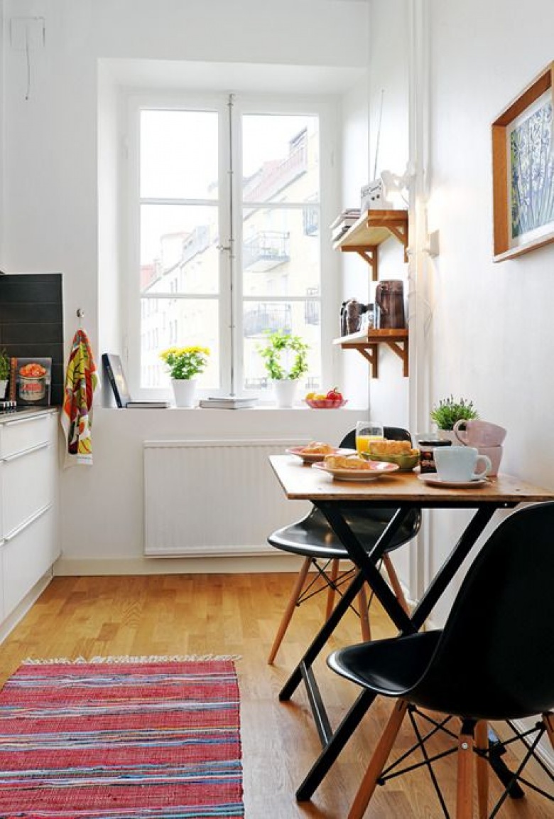 Niewielki stół w kuchni w stylu skandynawskim. Białe ściany i meble kuchenne stanowią tlo dla stolika i krzeseł...