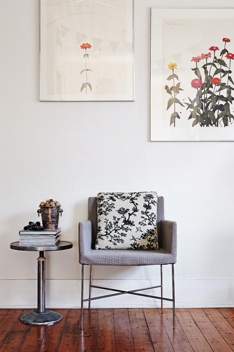 Nowoczesny szary fotel na metalowych nogach, okragły stolik pomocniczy i kolorowe artprinty na białej ścianie (24756)