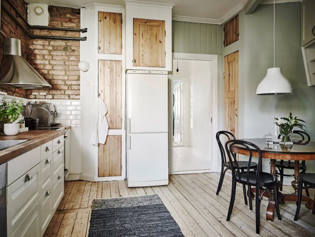 Jasne drewniane szafki i podłoga przy białej kuchni i zielonkawych ścianach dodaja przytulności.