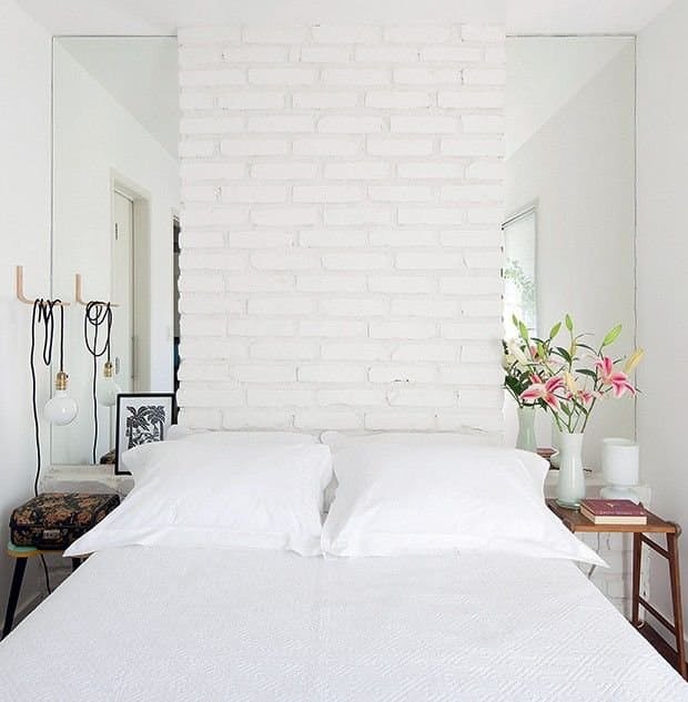Ściana z białych cegieł za łóżkiem w sypialni nawiązuje do stylu skandynawskiego. Świeże kwiaty w wazonie wprowadzają...