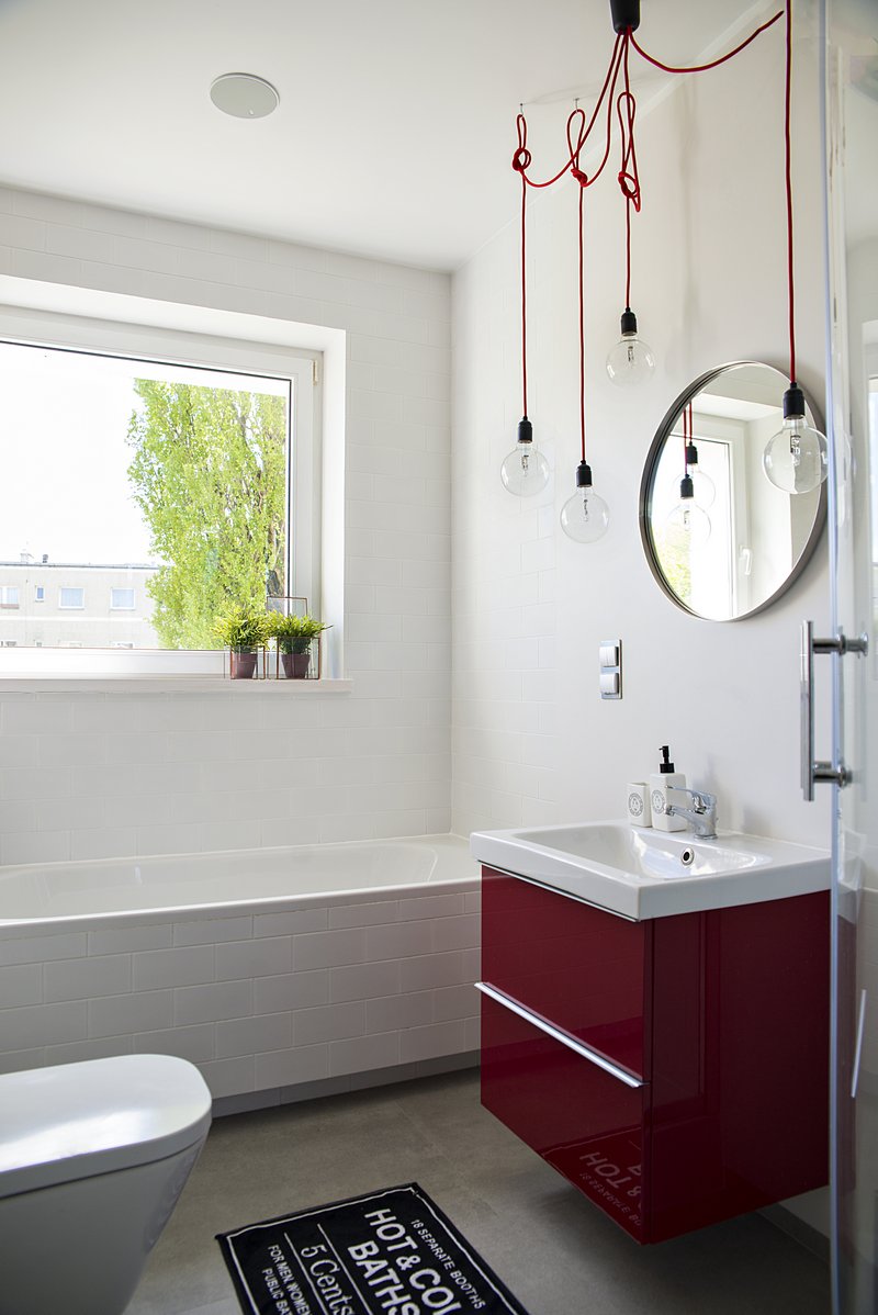 W łazience znajdują się zdecydowane akcenty w czerwieni, czyli szafka pod umywalką w wysokim połysku i oryginalna lampa...