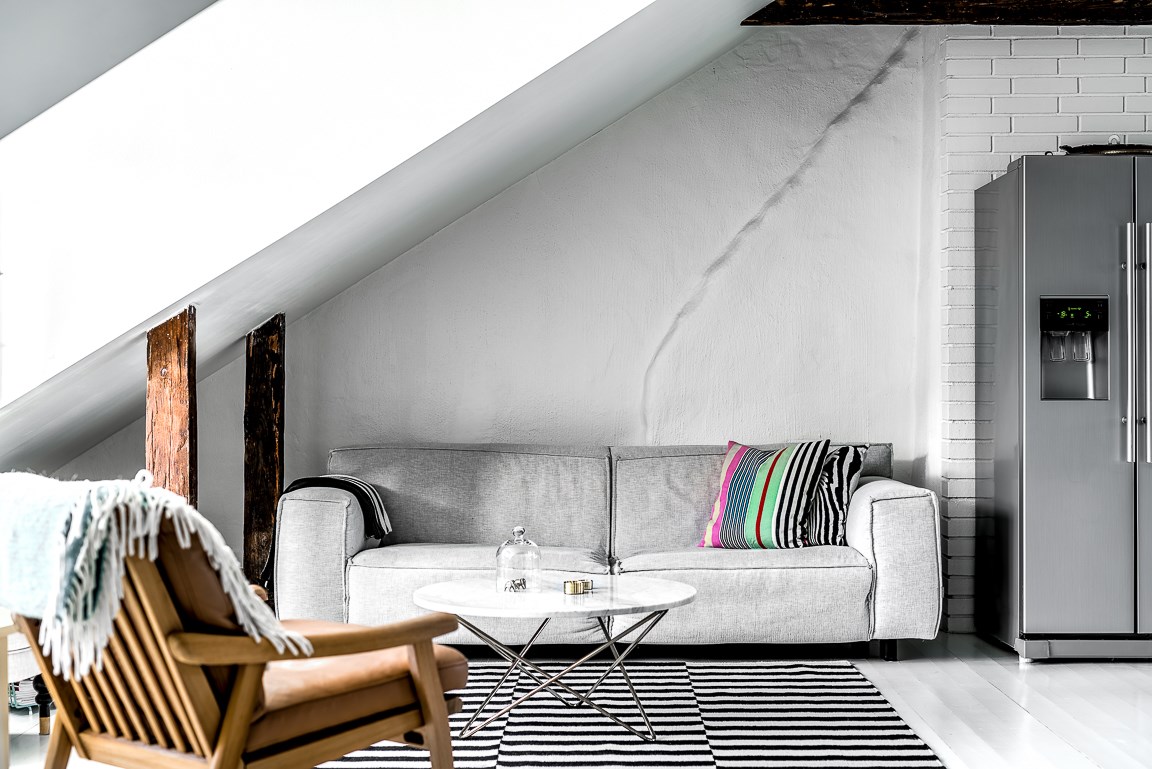 Szara sofa o prostej formie wydaje się idealnie komponować z ciekawą aranżacją wokół. Pasiasty dywan oraz poduszki...